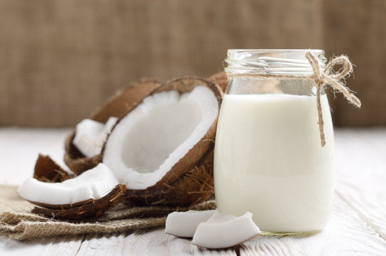 Glass jar of coconut milk with a halved coconut on a wooden surface